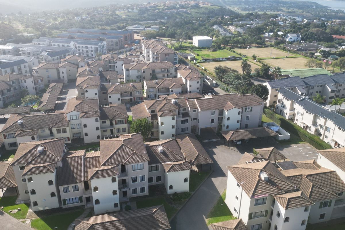 An aerial view of a residential apartment complex featuring multiple multi-story buildings with tiled roofs, paved driveways, and covered parking areas.