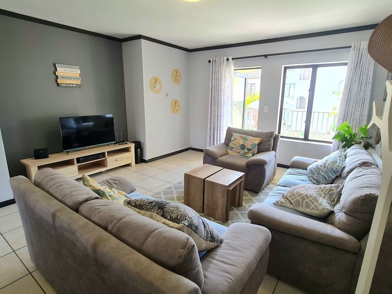 A comfortable living room featuring tiled flooring, neutral wall tones, and large windows that provide natural light and access to the exterior.