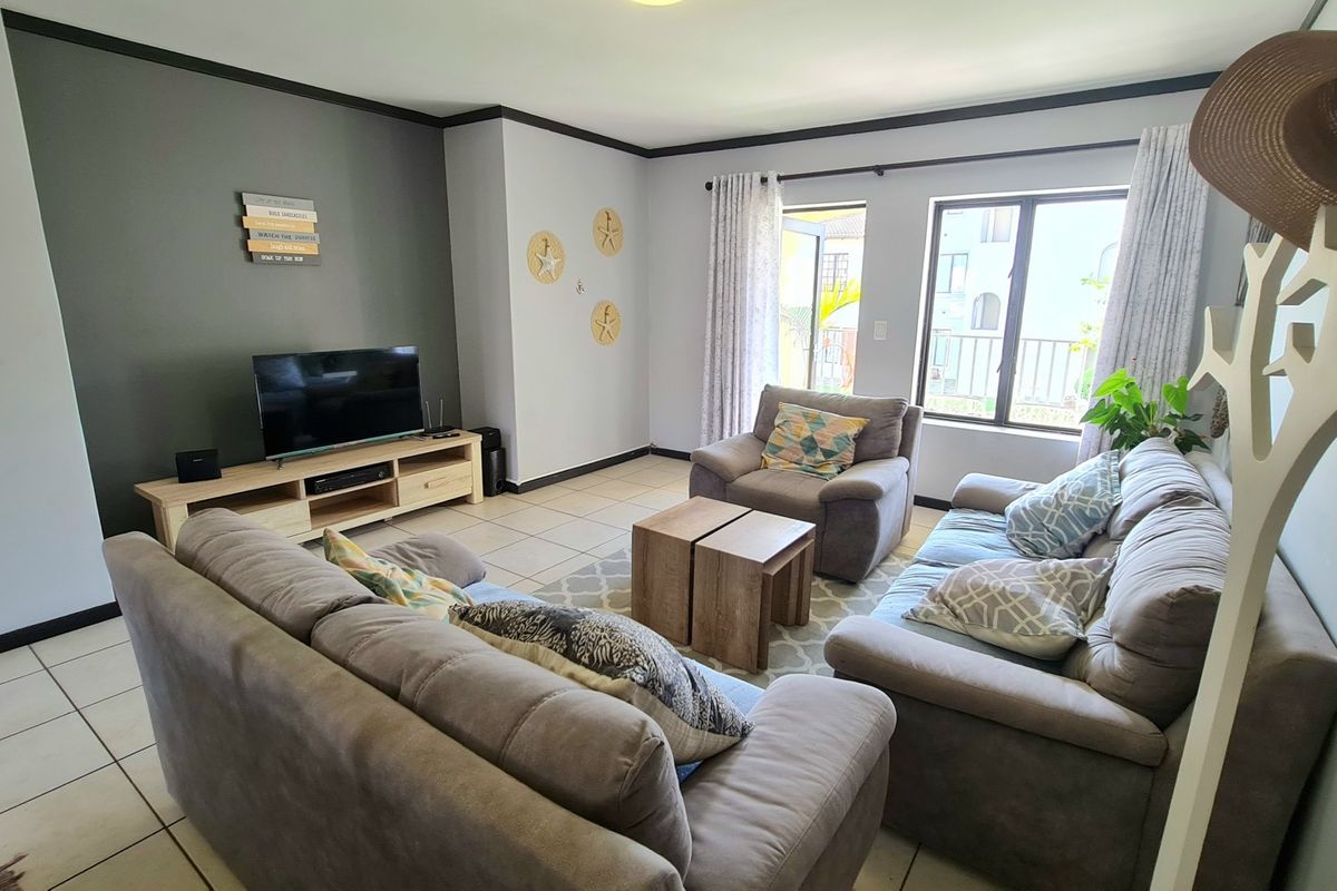 A comfortable living room featuring tiled flooring, neutral wall tones, and large windows that provide natural light and access to the exterior.