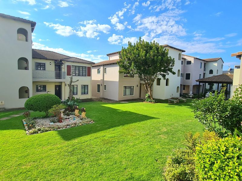 A well-maintained communal garden area featuring a lush lawn and landscaped beds, surrounded by multi-story apartment buildings with tiled roofs.