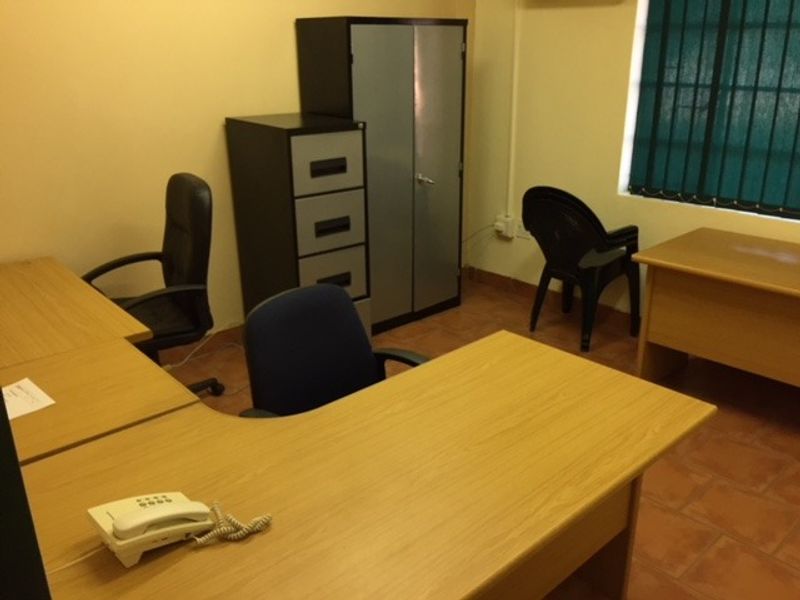 A functional office space featuring tiled flooring and a window fitted with security bars.