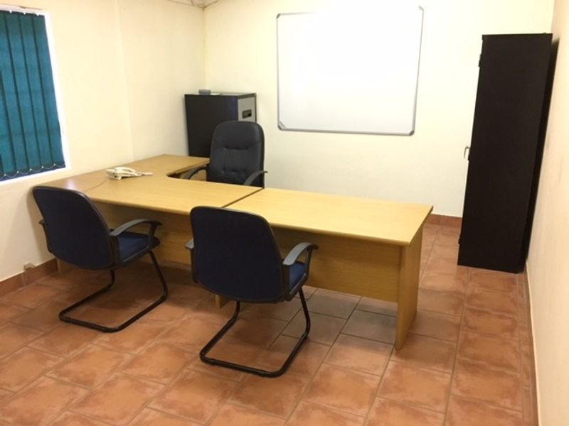 A functional office space featuring tiled flooring, vertical window blinds, and a wall-mounted whiteboard, suitable for professional use.