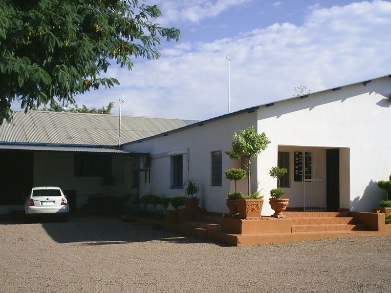 Front exterior view of the office building featuring a covered carport, tiled entrance steps, and a white facade with a corrugated metal roof.