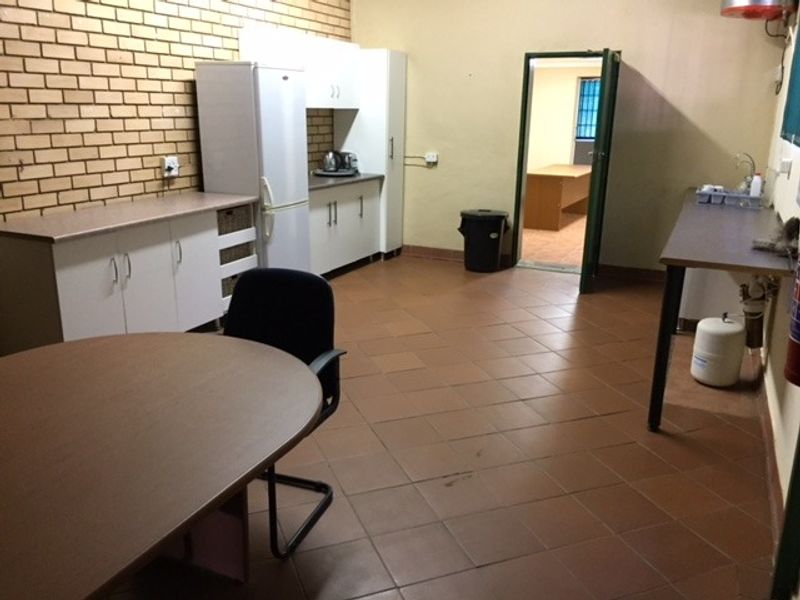 A functional office kitchenette featuring built-in cabinetry, laminate countertops, tiled flooring, and an exposed brick feature wall.
