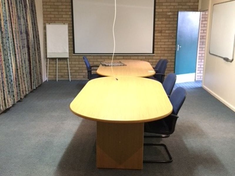 A functional office meeting room featuring exposed brick walls, a projector screen, ceiling-mounted projector, and split-system air conditioning.