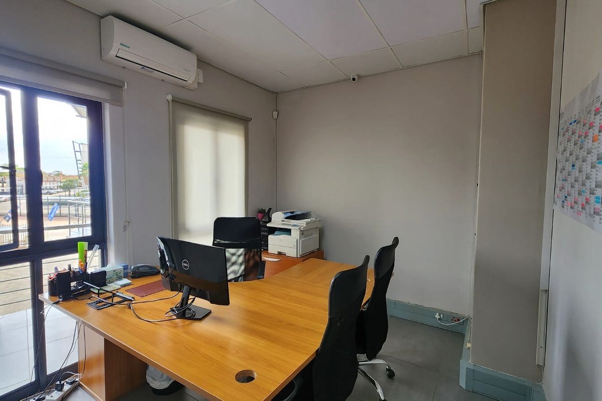 A functional office space featuring a suspended ceiling, split-system air conditioning, and large aluminium windows with roller blinds, providing ample natural light.
