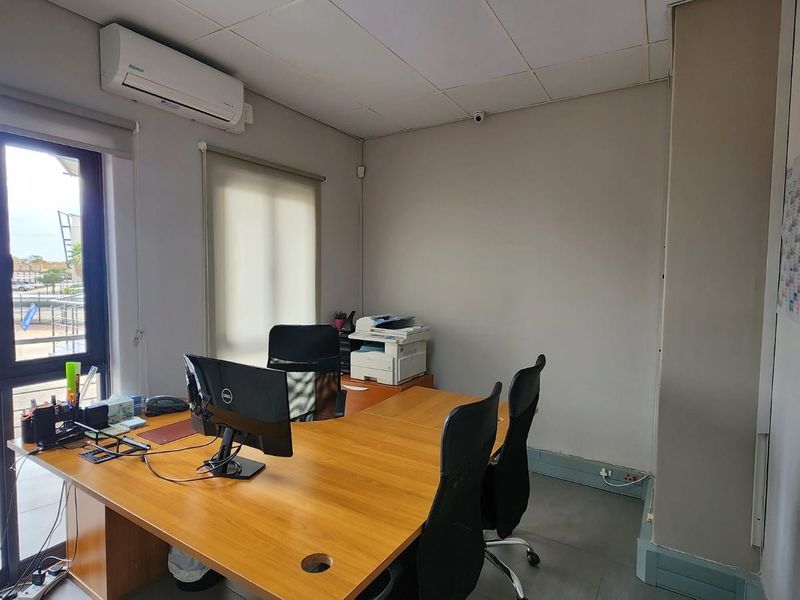 A functional office space featuring a suspended ceiling, split-system air conditioning, and large aluminium windows with roller blinds, providing ample natural light.