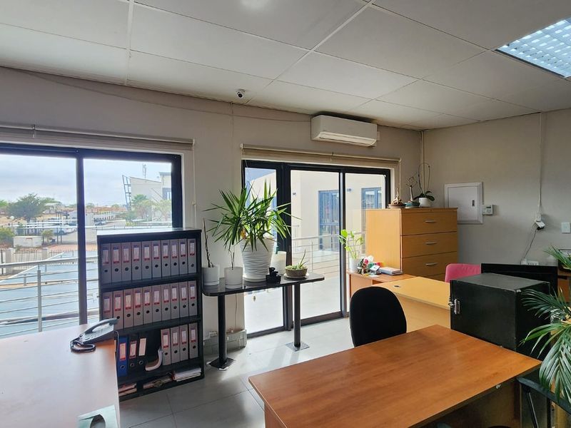 A functional office space featuring tiled flooring, suspended ceilings, split-system air conditioning, and large sliding glass doors providing natural light and exterior access.