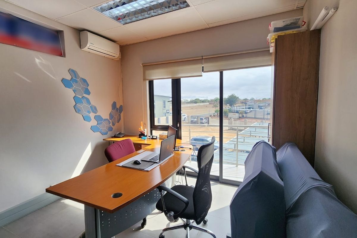 A functional office space featuring tiled flooring, air conditioning, and a large sliding glass door providing natural light and access to an exterior balcony.
