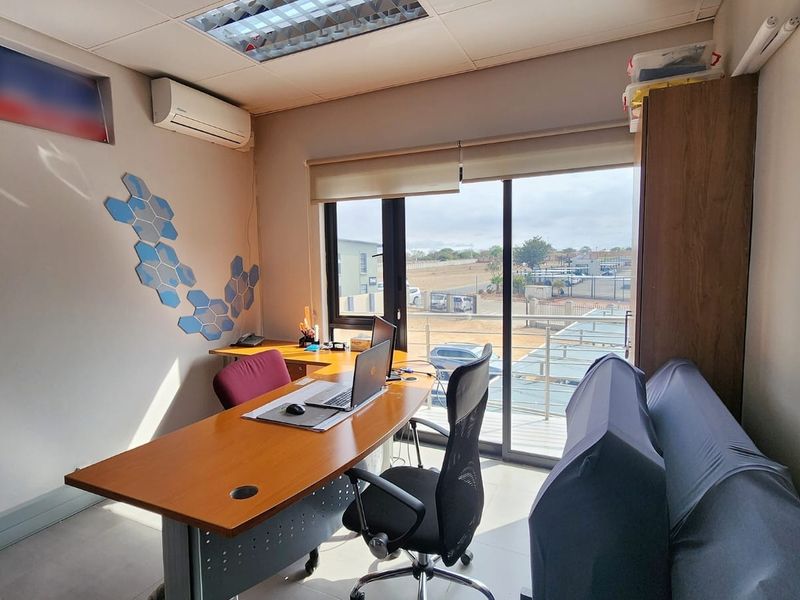 A functional office space featuring tiled flooring, air conditioning, and a large sliding glass door providing natural light and access to an exterior balcony.