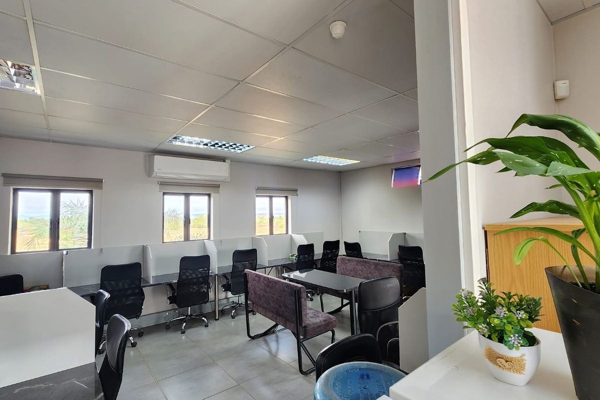 A functional office space featuring suspended ceilings, recessed lighting, wall-mounted air conditioning, and multiple built-in desk workstations with tiled flooring.