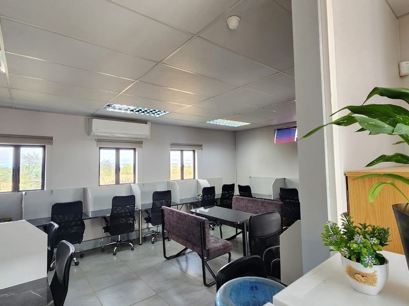 A functional office space featuring suspended ceilings, recessed lighting, wall-mounted air conditioning, and multiple built-in desk workstations with tiled flooring.