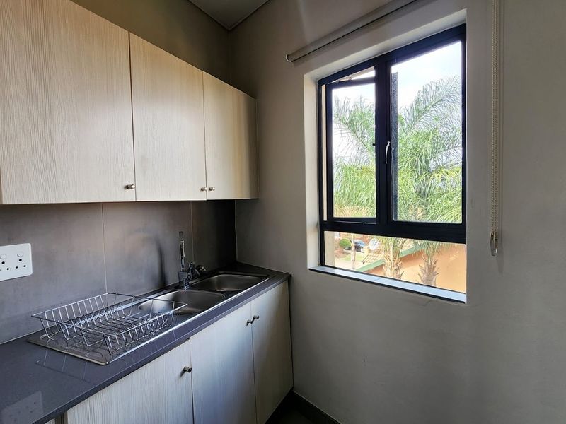 A clean and functional scullery area featuring modern light wood cabinetry, a stainless steel sink, and a dark stone countertop with a window view.