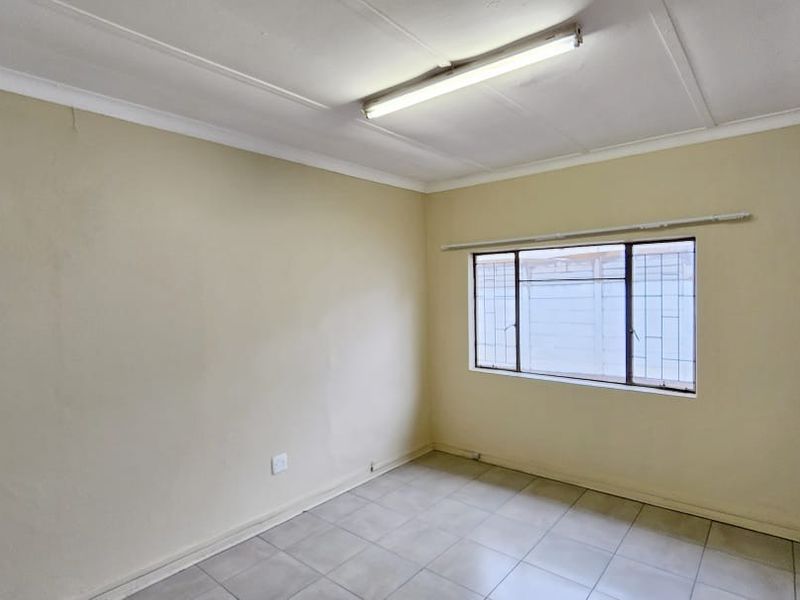 An empty office space featuring tiled flooring, a fluorescent light fixture, and a window fitted with security bars.