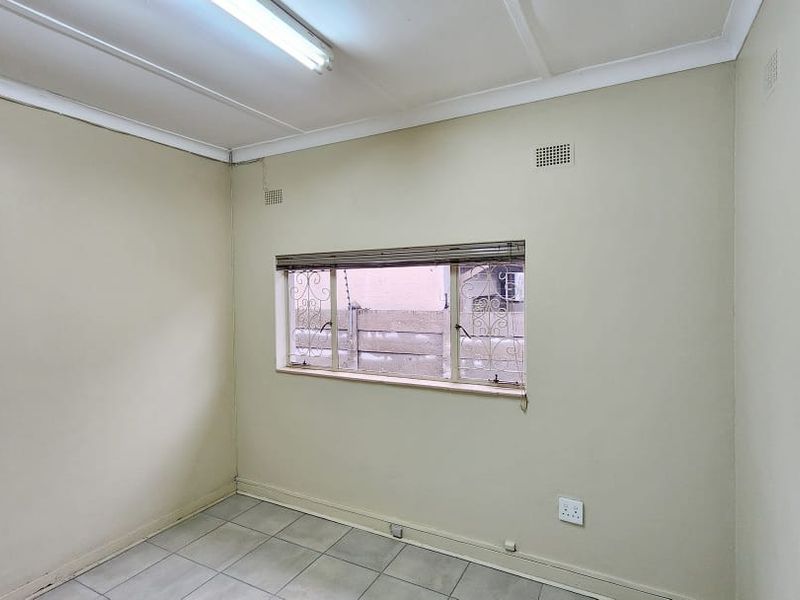 A vacant office space featuring tiled flooring, fluorescent lighting, and a window with security bars, ready for customization.
