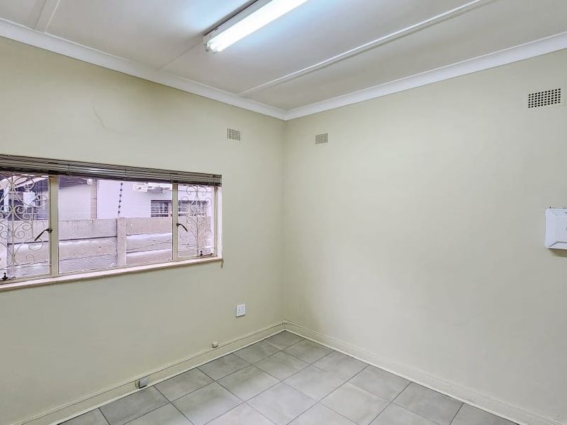 A functional, empty office space featuring tiled flooring, a window with security bars, and surface-mounted electrical and network infrastructure.