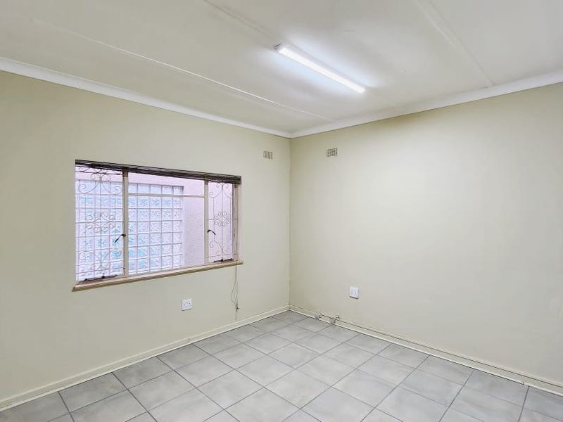 A vacant office space featuring tiled flooring, a fluorescent light fixture, and a window with security bars.