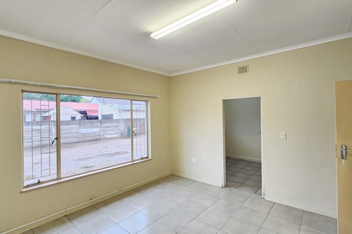 A vacant office space featuring tiled flooring, fluorescent lighting, and security bars on the window, offering a functional layout for a professional workspace.