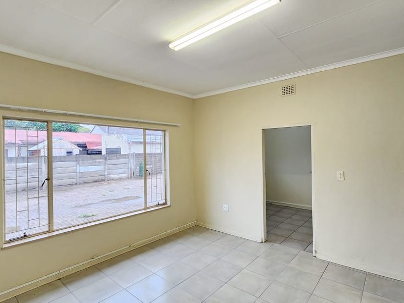 A vacant office space featuring tiled flooring, fluorescent lighting, and security bars on the window, offering a functional layout for a professional workspace.