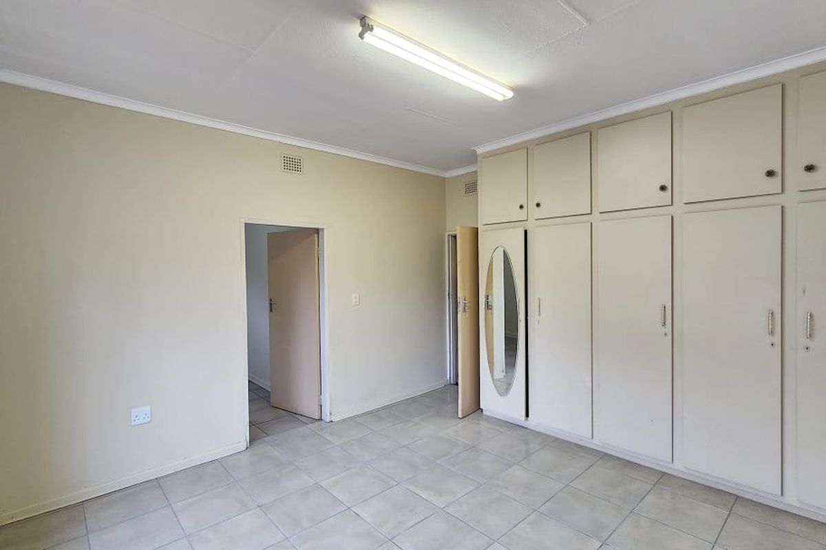 An empty office space featuring tiled flooring, neutral walls, and extensive built-in storage cupboards with integrated mirror detail.
