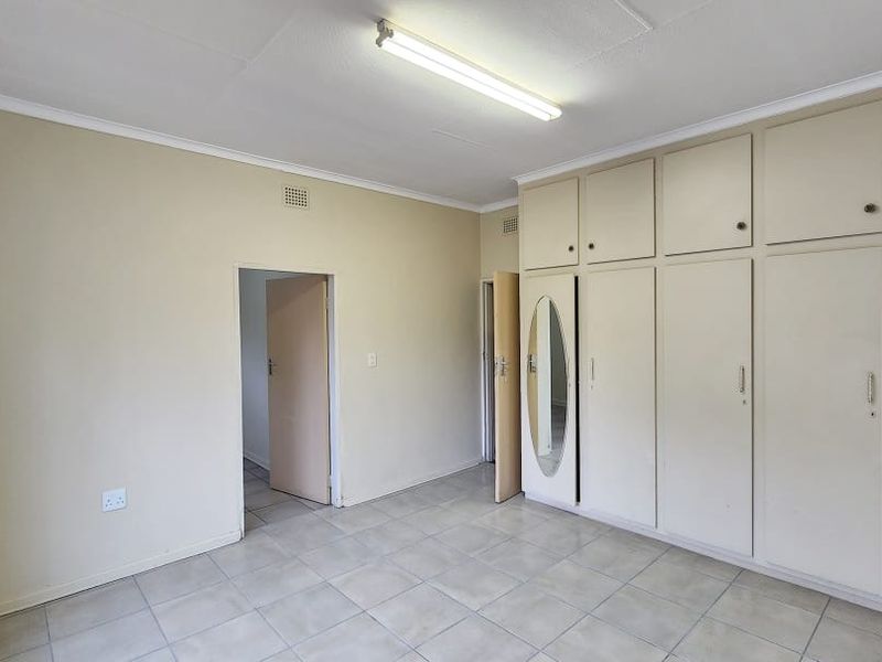 An empty office space featuring tiled flooring, neutral walls, and extensive built-in storage cupboards with integrated mirror detail.