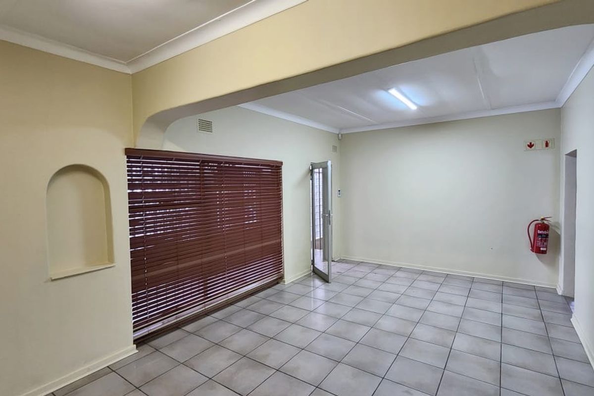 A bright, open-plan office space featuring tiled flooring, a decorative wall niche, and large windows with venetian blinds.