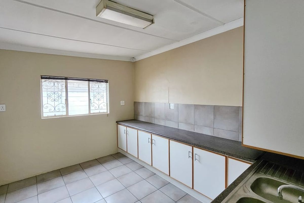 A functional, empty kitchen space featuring built-in cabinetry, a laminate countertop, a stainless steel sink, and tiled backsplash, ready for modernization.