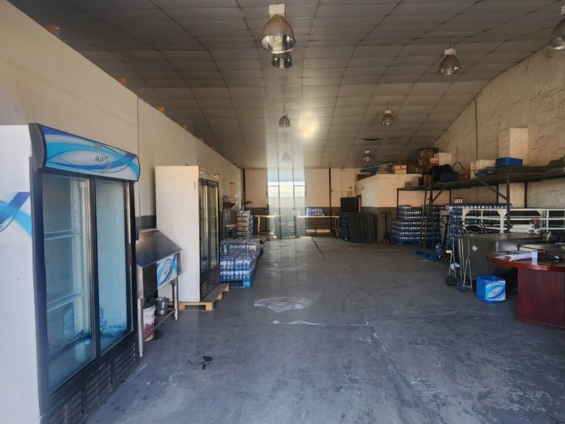 Spacious industrial utility area featuring concrete flooring, high ceilings with industrial lighting, and a secure entrance gate, suitable for storage or light manufacturing.