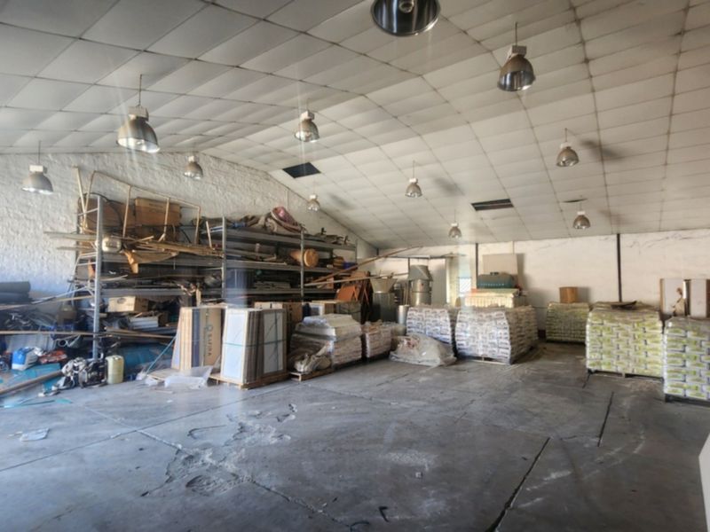 Spacious industrial utility area featuring concrete flooring, high ceilings with pendant lighting, and integrated metal shelving units suitable for storage or workshop use.