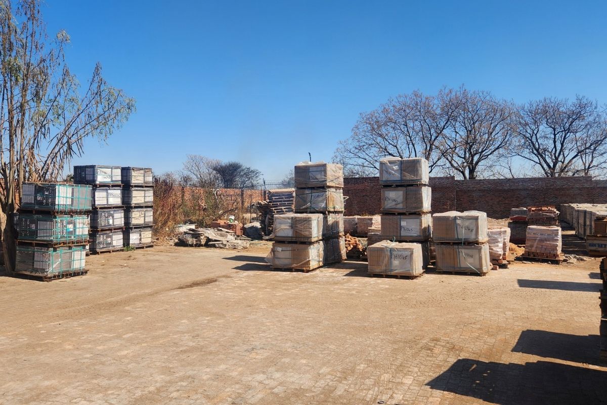 An industrial outdoor yard area featuring paved ground and a brick perimeter wall, currently used for storage of palletized materials.