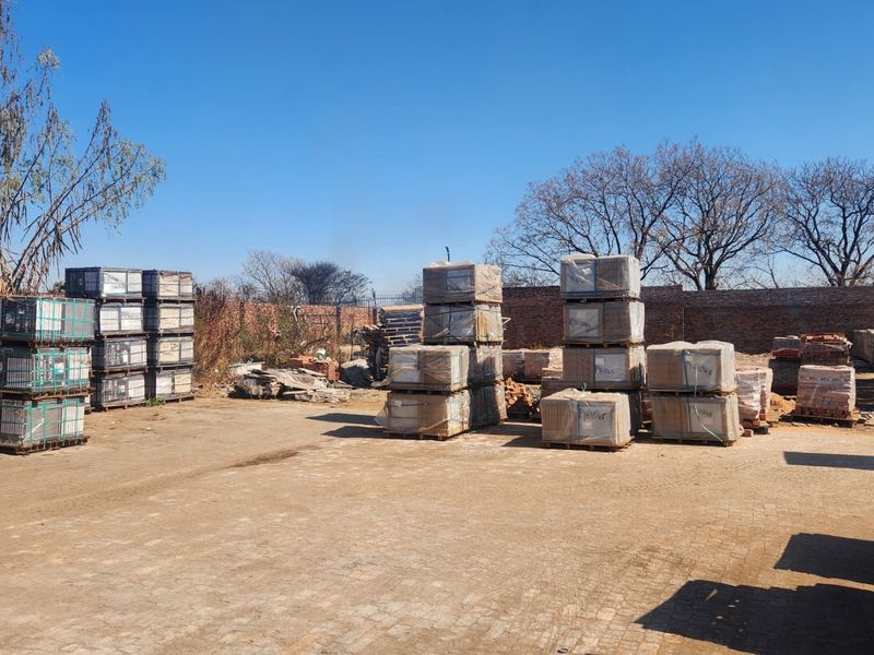 An industrial outdoor yard area featuring paved ground and a brick perimeter wall, currently used for storage of palletized materials.