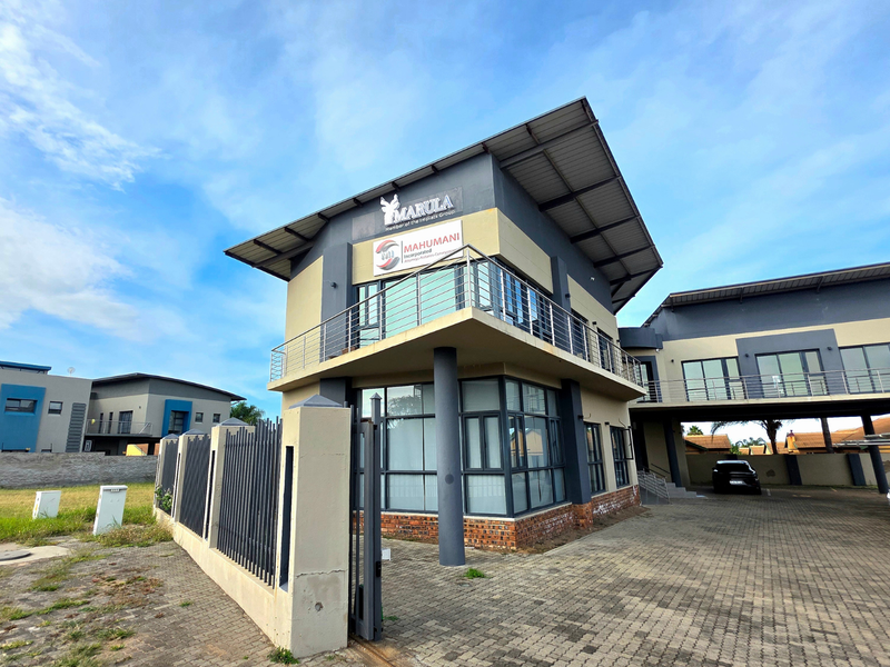 Modern two-story office building featuring a prominent balcony, aluminum window frames, and a paved driveway with secure perimeter fencing.
