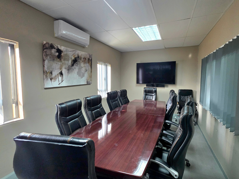 A professional office boardroom featuring a large conference table, wall-mounted television, split-system air conditioning, and vertical window blinds.