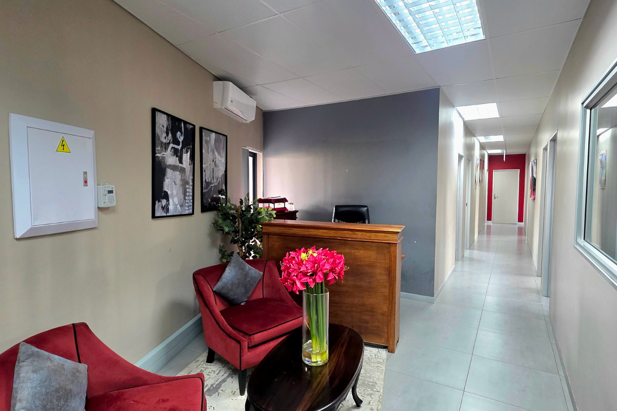 A professional office reception area featuring a built-in wooden desk, tiled flooring, recessed ceiling lighting, and a wall-mounted air conditioning unit.