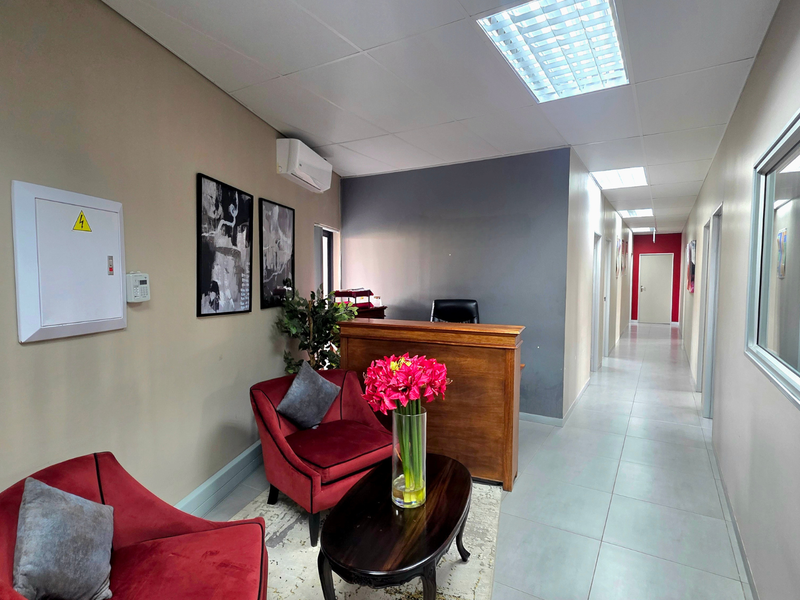 A professional office reception area featuring a built-in wooden desk, tiled flooring, recessed ceiling lighting, and a wall-mounted air conditioning unit.