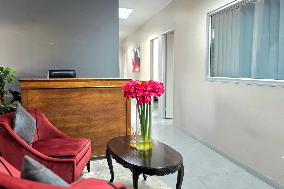 A professional office reception area featuring a wooden reception desk, tiled flooring, and a bright, clean interior layout with access to adjacent office spaces.