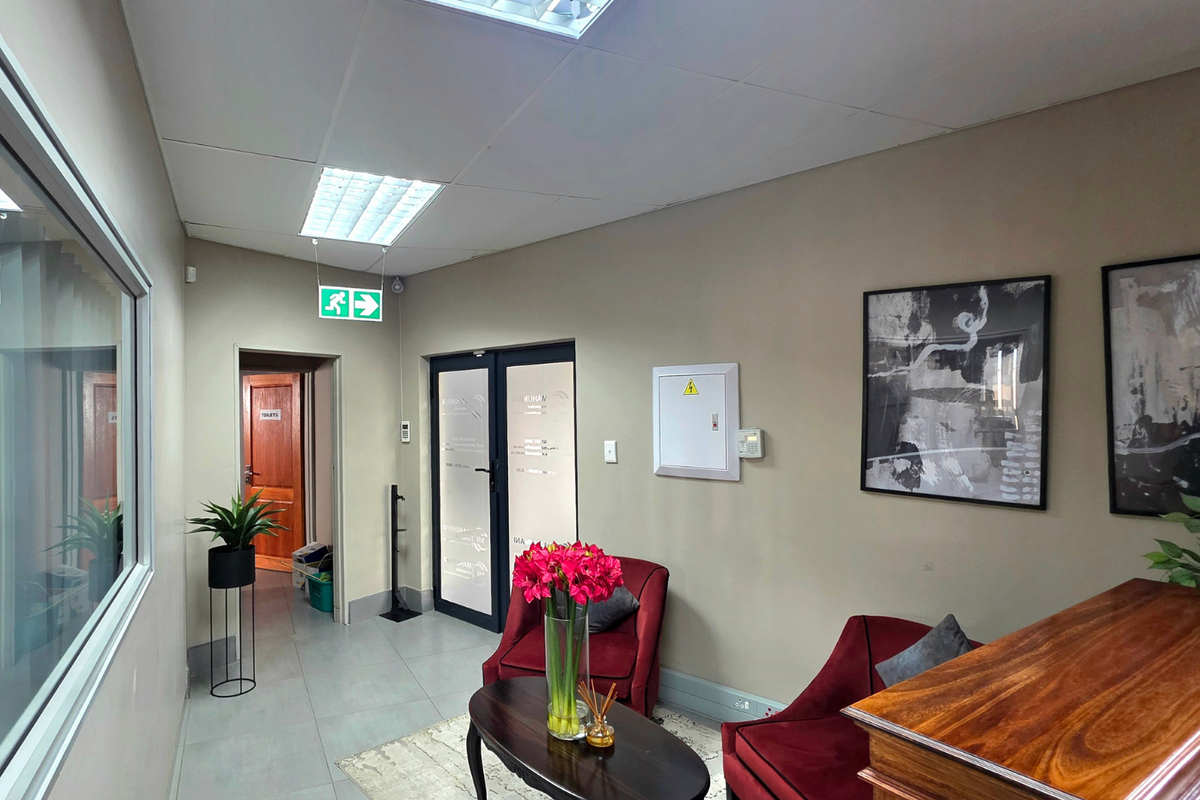 A professional office reception area featuring tiled flooring, recessed ceiling lighting, and a glass partition wall, providing a clean and functional workspace environment.