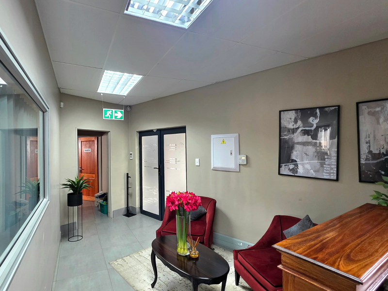 A professional office reception area featuring tiled flooring, recessed ceiling lighting, and a glass partition wall, providing a clean and functional workspace environment.