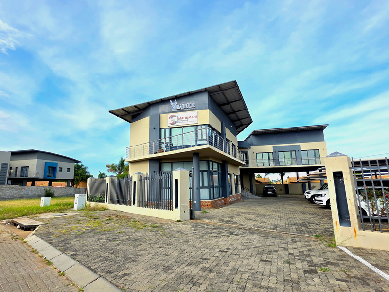 Front exterior view of a modern two-story office building featuring a paved driveway, metal perimeter fencing, and a balcony with glass sliding doors.