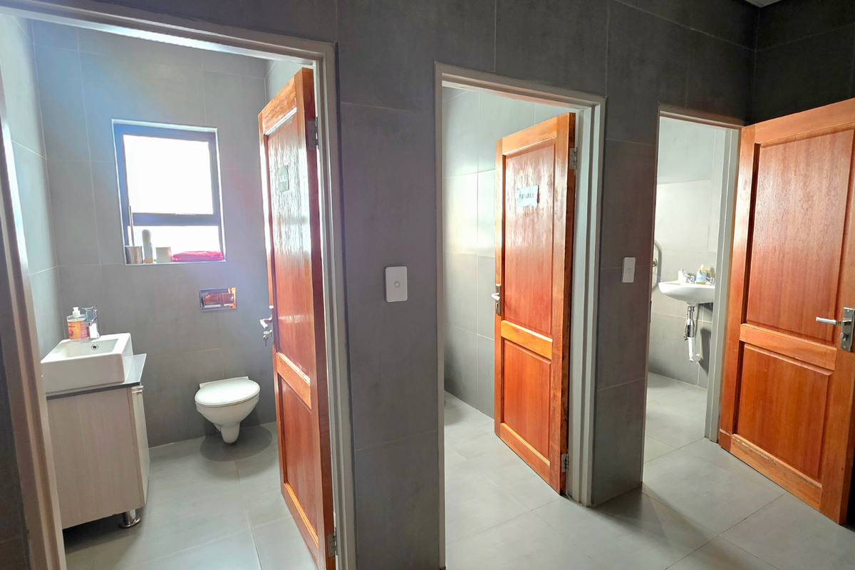 A clean office bathroom facility featuring multiple private stalls with timber doors, wall-mounted toilets, and modern vanity basins with tiled finishes.