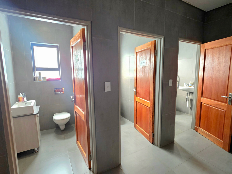 A clean office bathroom facility featuring multiple private stalls with timber doors, wall-mounted toilets, and modern vanity basins with tiled finishes.