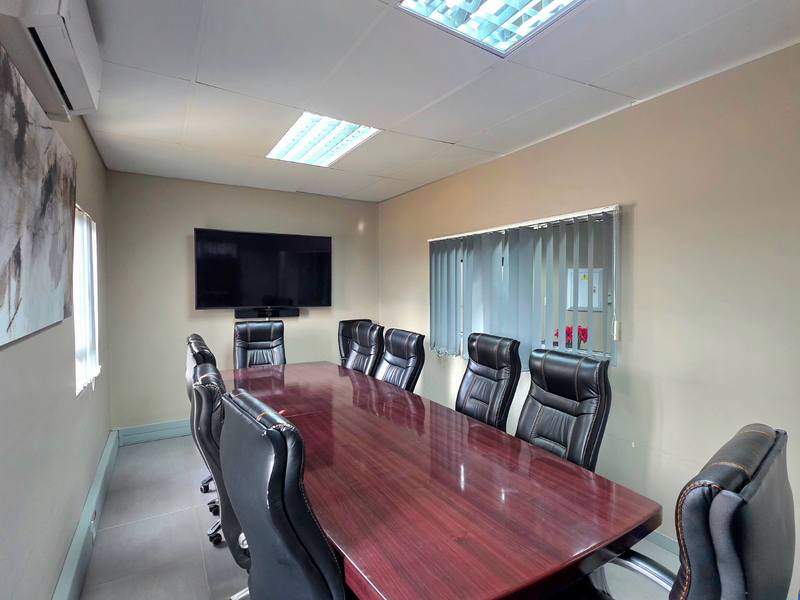 A professional boardroom featuring tiled flooring, suspended ceiling with recessed lighting, wall-mounted air conditioning, and vertical blinds.