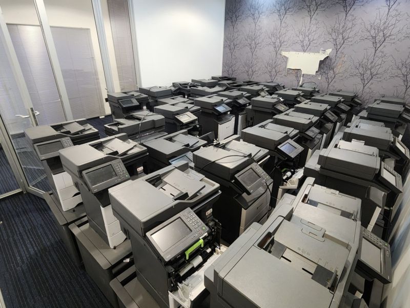 An office space currently utilized for storage, featuring carpeted flooring, glass partitioning, and a feature wall with patterned wallpaper.