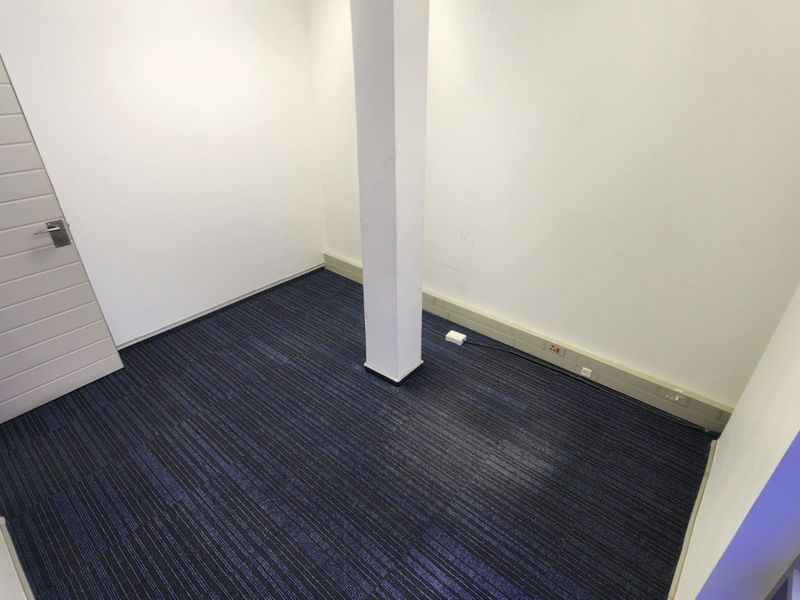 A clean, empty office space featuring dark blue carpet tiles, a central structural column, and white walls.