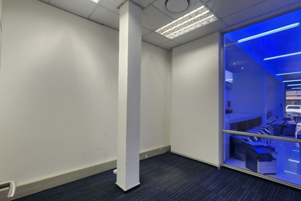 An empty office space featuring a structural column, carpeted flooring, suspended ceiling with recessed lighting, and a large glass partition wall.