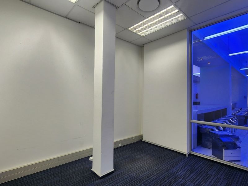 An empty office space featuring a structural column, carpeted flooring, suspended ceiling with recessed lighting, and a large glass partition wall.
