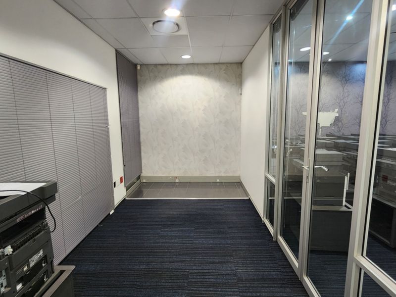 A clean, modern office space featuring glass partition walls, carpeted flooring, and a suspended ceiling with recessed lighting.