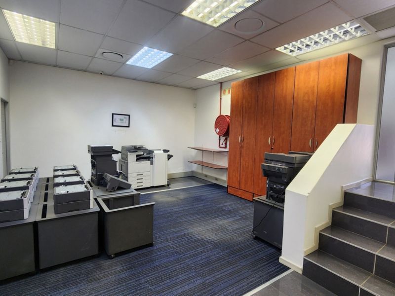 Functional office space featuring a suspended ceiling, built-in storage cabinetry, carpeted flooring, and direct access to a staircase.