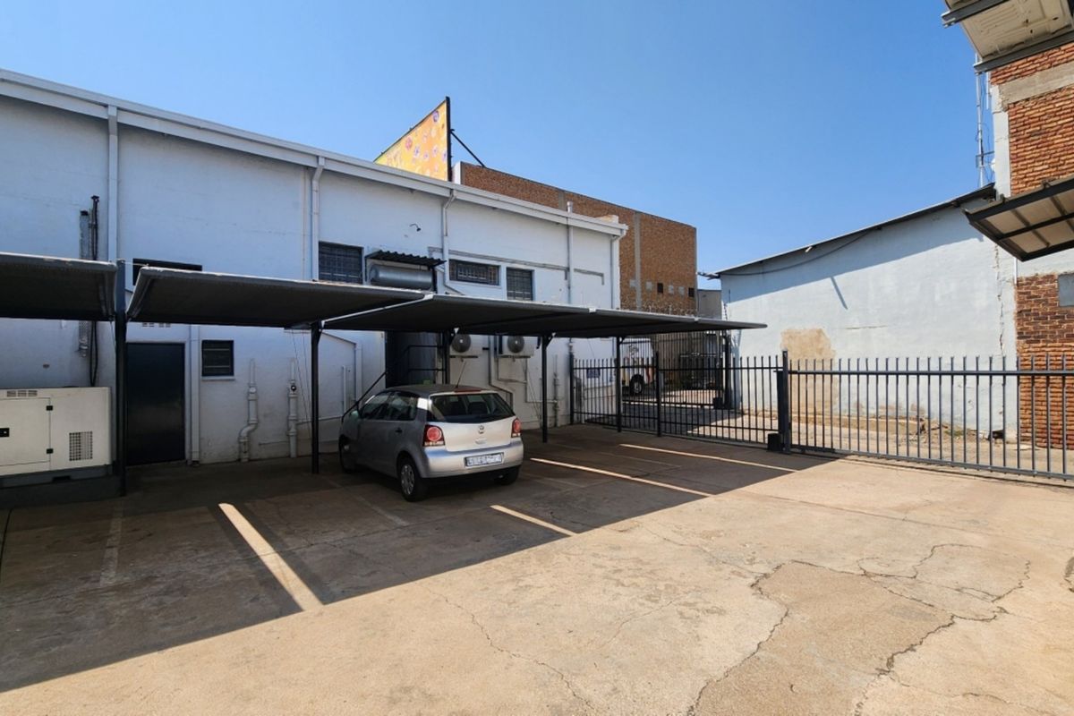 Rear exterior area featuring a concrete paved yard, shade cloth carport, security fencing, and external utility infrastructure.