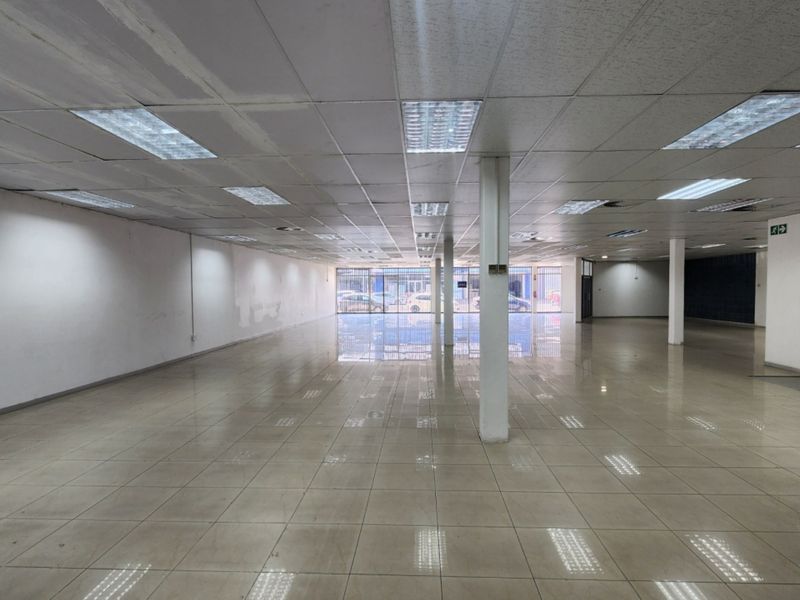 A spacious, empty open-plan retail unit featuring ceramic tile flooring, a suspended ceiling with recessed lighting, and a secure vault door.